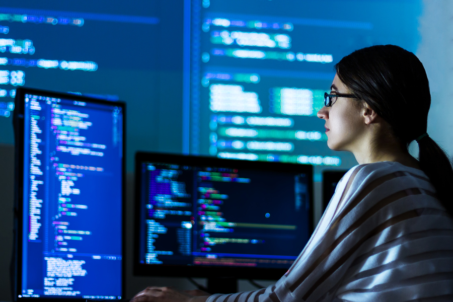 Young Women in Technology - A woman in glasses works with program code C++ Java Javascript on wide displays at night.